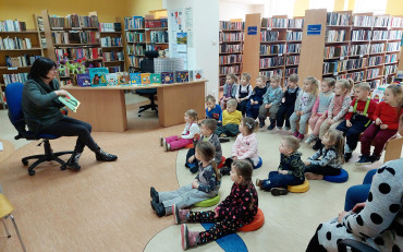 Na zdjęciu Wiola prezentuje dzieciom siędzącym na podłodze, książkę pt. Wszyscy ziewają