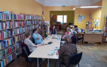 Panie wraz z bibliotekarką siedzą przy stole i dyskusują na temat książki