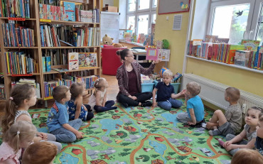 Dzieci siedzą w kole, bibliotekarka czyta książkę 