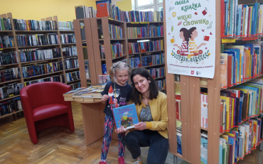 Dzieczynka wraz z bibliotekarkami pokazuje książkę, kartę i zakładkę do książki