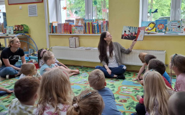 Pani bibliotekarka czyta książkę przedszkolakom, siedzącym w kółeczku na dywanie