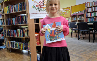 Dziewczynka pokazuje książkę, kartę i zakładkę do książki z akcji 