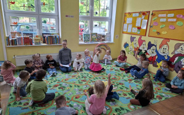 Bibliotekarka razem z dziećmi siedzi w kole na dywanie