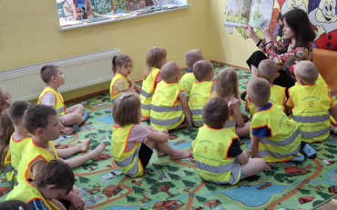 Dzieci siedzą na kolorowym dywanie, a bibliotekarka pokazuje obrazek
