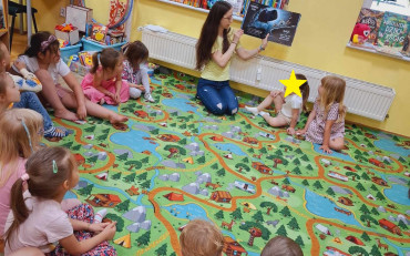 Bibliotekarka czyta dzieciom księżeczkę, dzieci siedzą w kole na dywanie