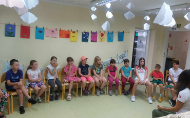 Dzieci siedzą na krzesłach a prowadząca opowiada o kameleonie