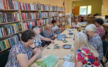 Panie siedzą przy stole, naradzają się i robią na drutach