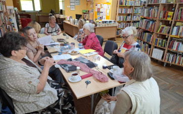 Panie siedzą przy stole i robią na drutach