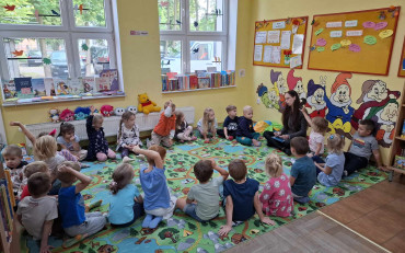 dzieci wraz z bibliotekarką siedzą w kole na dywanie