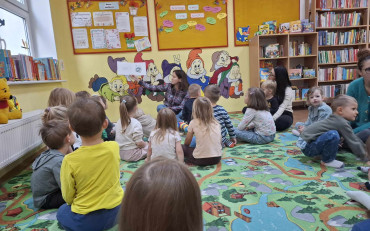 Bibliotekarka czyta dzieciom księżeczkę, dzieci siedzą w kole