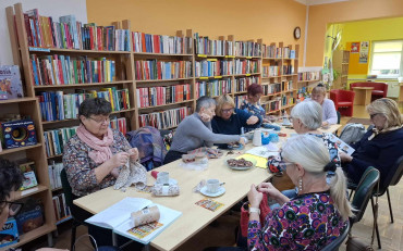 Panie siedzą przy stole, robią na drutach, rozmawiają