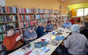 Panie siedza przy stole i robią na drutach