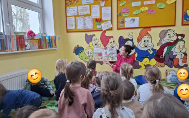 Bibliotekarka razem z dziećmi siedzi na dywanie i czyta książkę