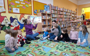 Bibliotekarka razem z dziećmi siedzi na dywanie i czyta książkę