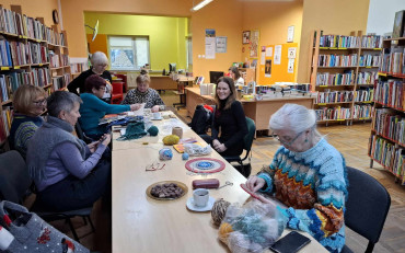 Panie siedza przy stole i robią na drutach