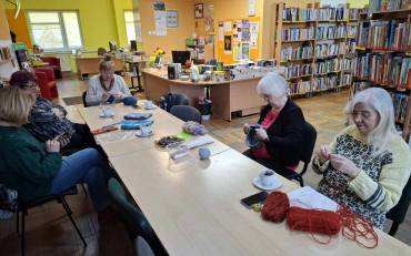 Panie siedzą przy stole, robią na drutach, rozmawiają